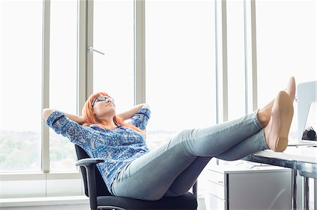 Full-length of businesswoman relaxing with feet up at desk in creative office Photographie de stock - Premium Libres de Droits, Code: 693-07912543