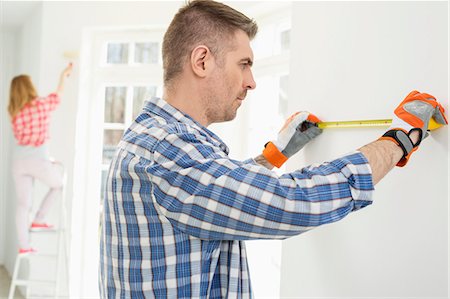 Man measuring wall with woman painting in background Stock Photo - Premium Royalty-Free, Code: 693-07912592