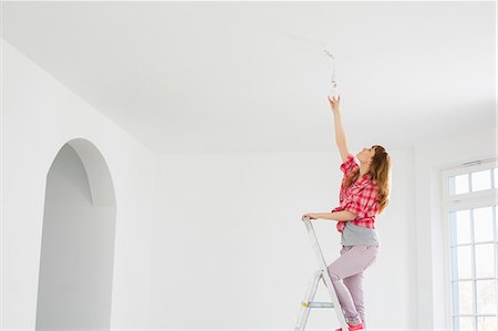 Full-length of woman on ladder fitting light bulb in new house Photographie de stock - Premium Libres de Droits, Code: 693-07912619