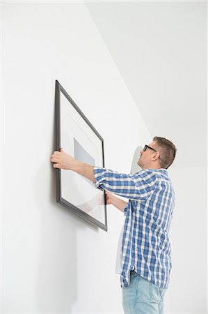 simsearch:693-07912604,k - Man positioning picture frame on wall Photographie de stock - Premium Libres de Droits, Code: 693-07912627