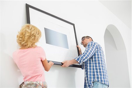Couple hanging picture frame on wall in new house Foto de stock - Sin royalties Premium, Código: 693-07912628