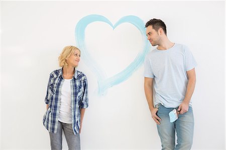 Mid-adult couple looking at each other with painted heart on wall Stock Photo - Premium Royalty-Free, Code: 693-07912647