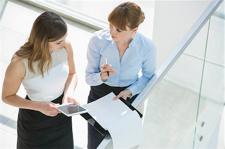 High angle view of businesswomen discussing over tablet PC and documents by railing in office Stock Photo - Premium Royalty-Free, Code: 693-07912721