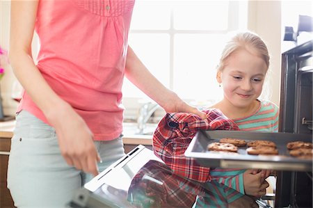 Smiling looking at mother removing cookie tray from oven at home Stock Photo - Premium Royalty-Free, Code: 693-07912797