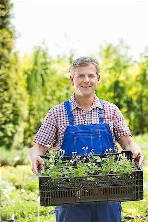 simsearch:6102-03905363,k - Portrait of smiling man holding crate of potted plants at garden Stock Photo - Premium Royalty-Free, Code: 693-07912846