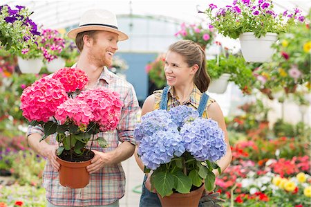 Happy gardeners looking at each other while holding flower pots at greenhouse Stock Photo - Premium Royalty-Free, Code: 693-07912907