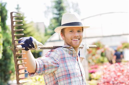 Portrait of smiling gardener carrying rake on shoulders at plant nursery Stock Photo - Premium Royalty-Free, Code: 693-07912900