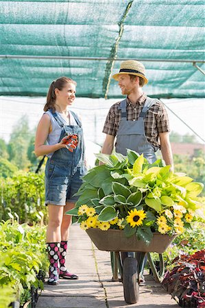 simsearch:693-07912856,k - Smiling gardeners discussing while pushing plants in wheelbarrow at greenhouse Stock Photo - Premium Royalty-Free, Code: 693-07912928