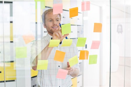 Young businessman reading sticky paper on glass wall at creative office Stock Photo - Premium Royalty-Free, Code: 693-07912955