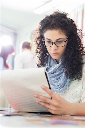 simsearch:693-07913057,k - Young businesswoman reading notepad at creative office with colleagues in background Photographie de stock - Premium Libres de Droits, Code: 693-07912963