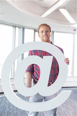 simsearch:693-07912497,k - Portrait of confident businessman holding at sign in creative office Foto de stock - Sin royalties Premium, Código: 693-07912983