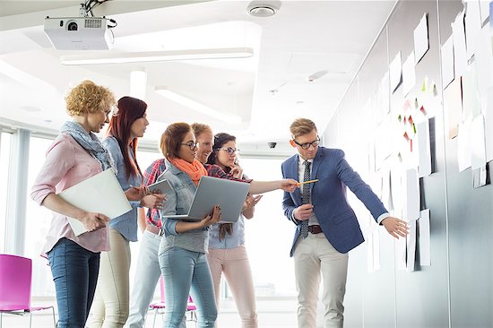 Creative businesspeople discussing over documents on wall in office Stock Photo - Premium Royalty-Free, Image code: 693-07913007