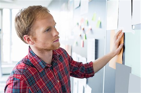 paper on wall - Young businessman reading documents on wall at creative office Stock Photo - Premium Royalty-Free, Code: 693-07913048