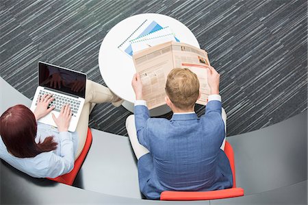High angle view of businessman reading newspaper while female colleague using laptop in office Stock Photo - Premium Royalty-Free, Code: 693-07913051