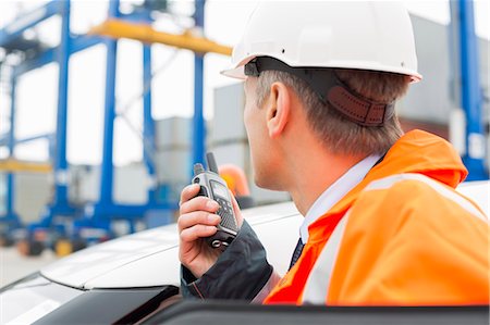 Middle-aged man using walkie-talkie while standing beside car in shipping yard Photographie de stock - Premium Libres de Droits, Code: 693-07913083