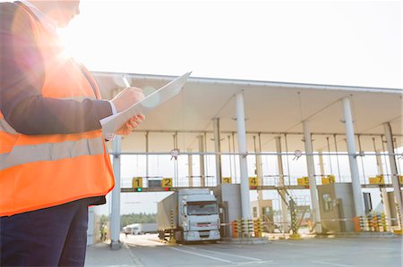 Midsection of female worker writing on clipboard while looking at truck entering in shipping yard Stock Photo - Premium Royalty-Free, Code: 693-07913154