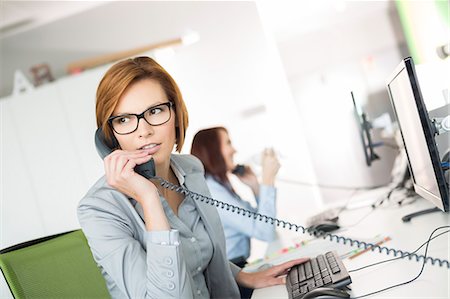 simsearch:693-07913272,k - Young businesswoman talking on telephone at desk in office Photographie de stock - Premium Libres de Droits, Code: 693-07913220