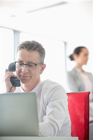 simsearch:693-07913272,k - Businessman talking on telephone with colleague in background at office Photographie de stock - Premium Libres de Droits, Code: 693-07913250