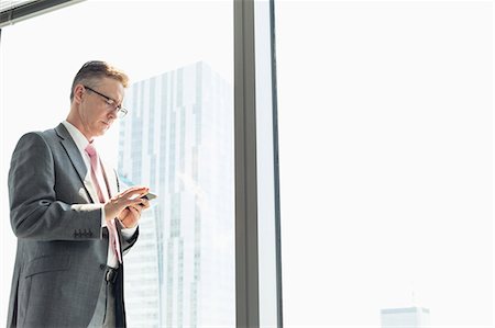 simsearch:693-08769593,k - Mature businessman using cell phone by window Stock Photo - Premium Royalty-Free, Code: 693-07913275