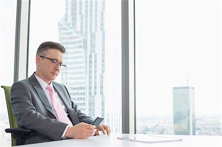 Mature businessman text messaging through cell phone near office window Stock Photo - Premium Royalty-Free, Code: 693-07913291