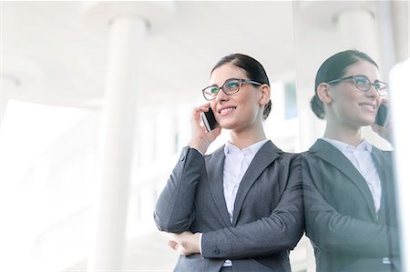 simsearch:693-06403498,k - Happy businesswoman using cell phone while leaning on glass wall Stock Photo - Premium Royalty-Free, Code: 693-08126996