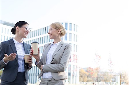 simsearch:693-08127175,k - Happy businesswomen conversing while holding disposable cups outside office building Fotografie stock - Premium Royalty-Free, Codice: 693-08127006