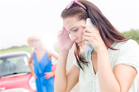 forehead - Worried woman using mobile phone while friend standing by broken down car on sunny day Stock Photo - Premium Royalty-Free, Code: 693-08127074