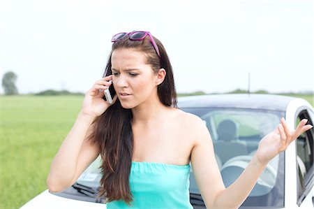 Frustrated woman using cell phone against broken down car Stock Photo - Premium Royalty-Free, Code: 693-08127070