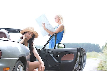 Woman using cell phone in convertible while friend reading map on road Stock Photo - Premium Royalty-Free, Code: 693-08127086