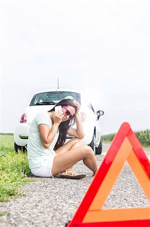 simsearch:693-08127130,k - Tensed woman using cell phone while sitting on country road by broken down car Stock Photo - Premium Royalty-Free, Code: 693-08127134