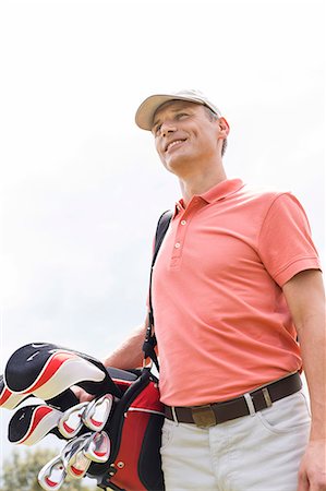 simsearch:693-06668077,k - Happy middle-aged man looking away while carrying golf bag against clear sky Fotografie stock - Premium Royalty-Free, Codice: 693-08127216