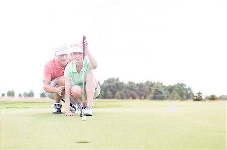 simsearch:649-08422474,k - Man assisting woman aiming ball on golf course against clear sky Stock Photo - Premium Royalty-Free, Code: 693-08127250