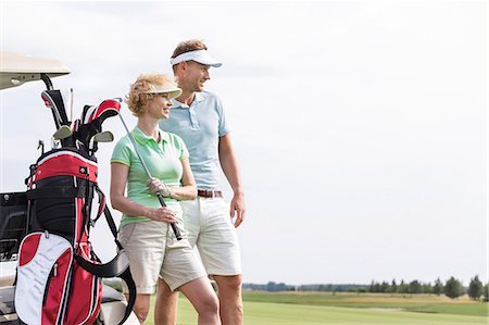 simsearch:693-08127426,k - Smiling man and woman standing at golf course against clear sky Stock Photo - Premium Royalty-Free, Code: 693-08127260