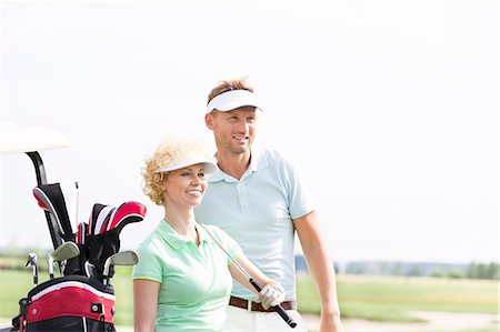 simsearch:693-06668077,k - Smiling golfers standing at golf course against clear sky Fotografie stock - Premium Royalty-Free, Codice: 693-08127261