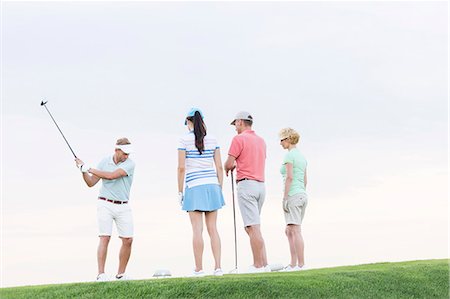 simsearch:693-06668077,k - Group of friends looking at man playing golf against clear sky Fotografie stock - Premium Royalty-Free, Codice: 693-08127288