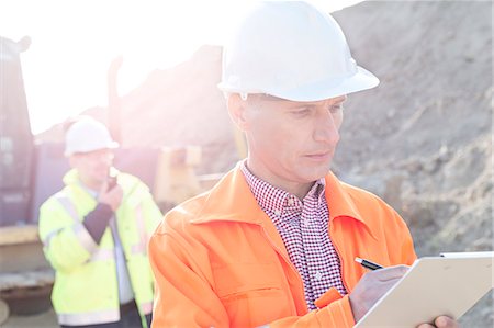 simsearch:693-08127800,k - Engineer writing on clipboard at construction site with colleague in background Stock Photo - Premium Royalty-Free, Code: 693-08127753