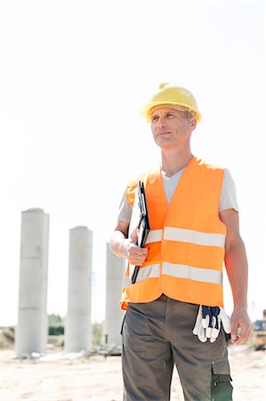 Thoughtful architect looking away while holding clipboard at construction site Foto de stock - Sin royalties Premium, Código: 693-08127814