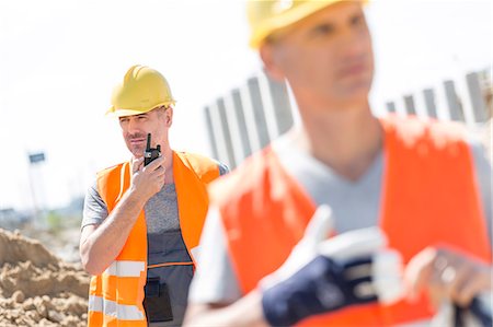 Middle-aged male worker using walkie-talkie with colleague in foreground at construction site Stock Photo - Premium Royalty-Free, Code: 693-08127823