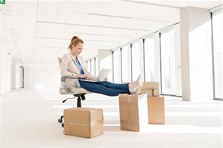 Full length of young businesswoman using laptop with feet up on cardboard box in new office Stock Photo - Premium Royalty-Free, Code: 693-08769208