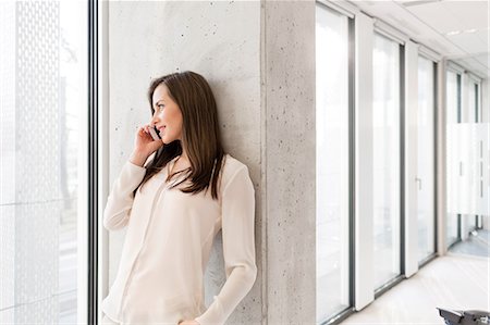 simsearch:693-08769320,k - Young businesswoman using mobile phone while leaning on wall in new office Stock Photo - Premium Royalty-Free, Code: 693-08769231