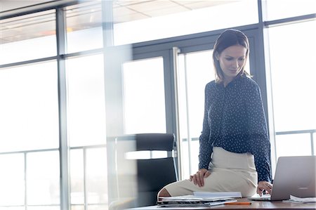 simsearch:693-08769320,k - Young businesswoman using laptop while sitting on desk in office Stock Photo - Premium Royalty-Free, Code: 693-08769311