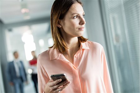 simsearch:693-08769289,k - Young businesswoman holding smart phone while looking away at office Stock Photo - Premium Royalty-Free, Code: 693-08769312