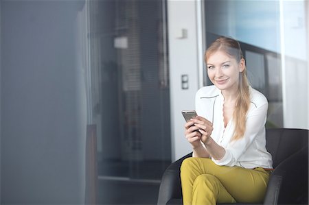 simsearch:693-08769320,k - Portrait of confident young businesswoman using mobile phone on chair in office Stock Photo - Premium Royalty-Free, Code: 693-08769320