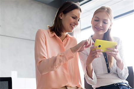 simsearch:693-08769289,k - Smiling young businesswomen using mobile phone in office Stock Photo - Premium Royalty-Free, Code: 693-08769336