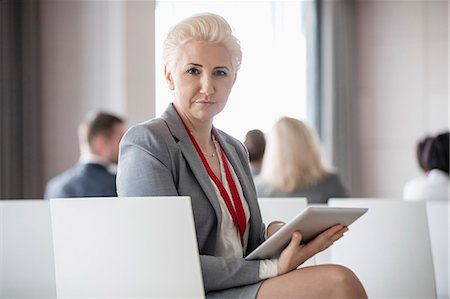 simsearch:693-08769426,k - Portrait of confident businesswoman holding digital tablet while sitting in seminar hall Stock Photo - Premium Royalty-Free, Code: 693-08769470