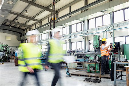 fabricación - Blurred motion of business people walking with manual worker in background at industry Foto de stock - Sin royalties Premium, Código: 693-08769497