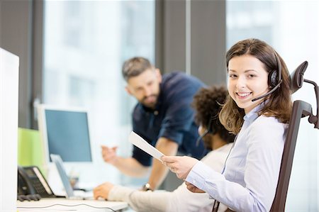 simsearch:693-08769593,k - Portrait of smiling customer service representative holding documents with colleagues in background at office Stock Photo - Premium Royalty-Free, Code: 693-08769542