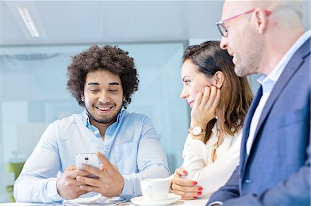 simsearch:693-08769320,k - Smiling young businessman using mobile phone with colleagues in office Stock Photo - Premium Royalty-Free, Code: 693-08769581