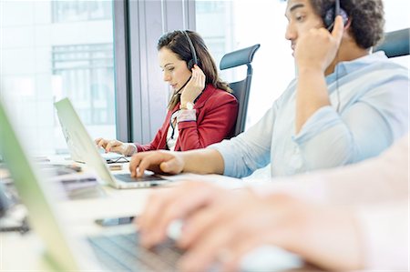 simsearch:693-08769320,k - Young businesswoman using headset and laptop with colleagues in foreground at office Stock Photo - Premium Royalty-Free, Code: 693-08769597