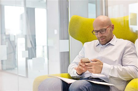 simsearch:693-08769320,k - Mid adult businessman using mobile phone while sitting on chair at office Stock Photo - Premium Royalty-Free, Code: 693-08769593